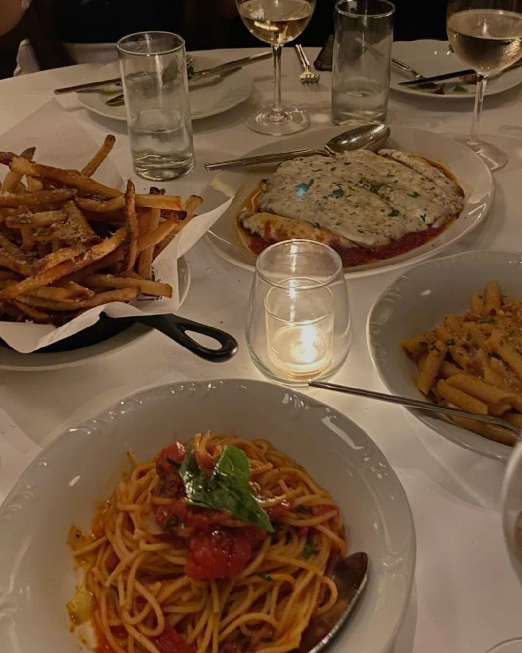Dinner table with plates of pasta, a side of fries, and glasses of water and wine.