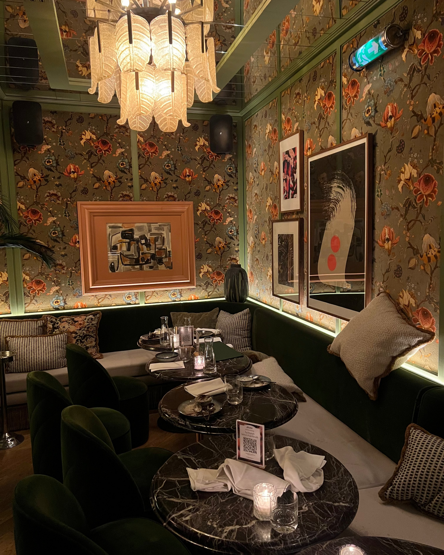 Decorative interior of a restaurant with floral wallpaper, framed pictures, and marble tables.